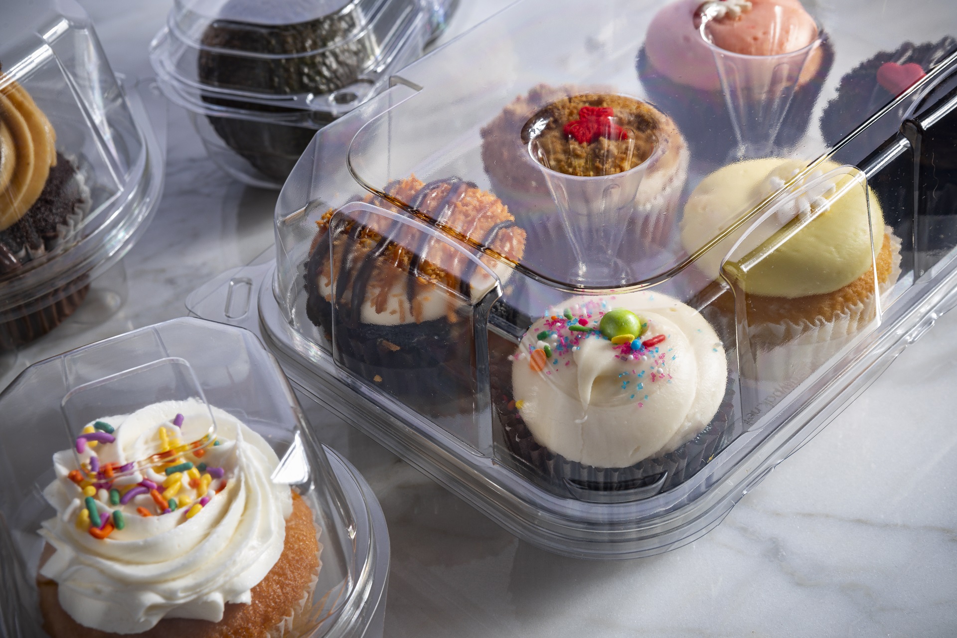 Clear bakery desserts container holding a variety of frosted cupcakes