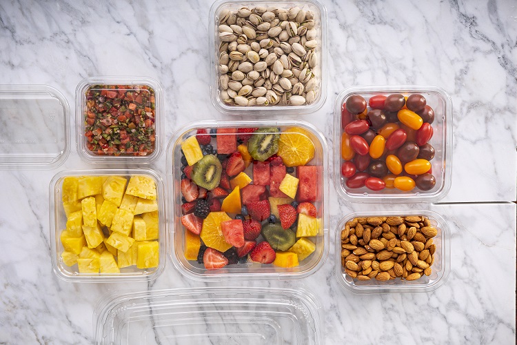 Assortment of clear square containers with tomatoes, fruit, and a variety of nuts