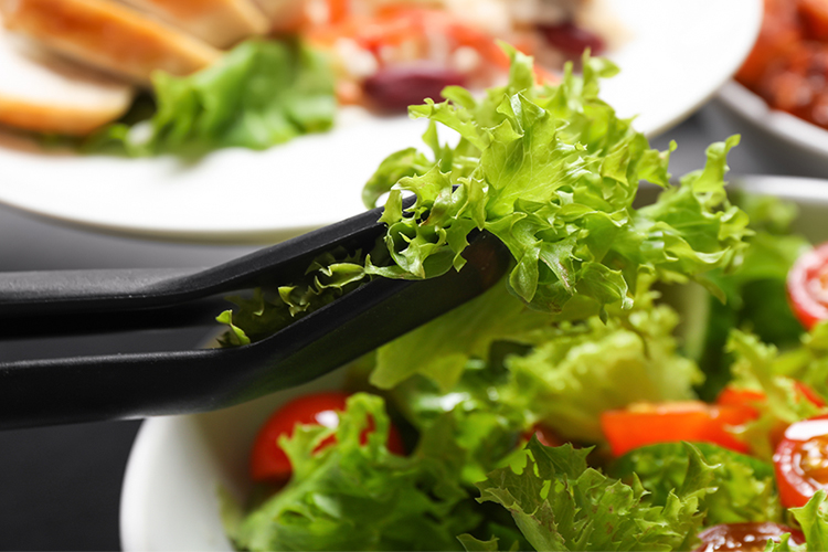 Black salad tong utensils picking up lettuce from a salad bowl